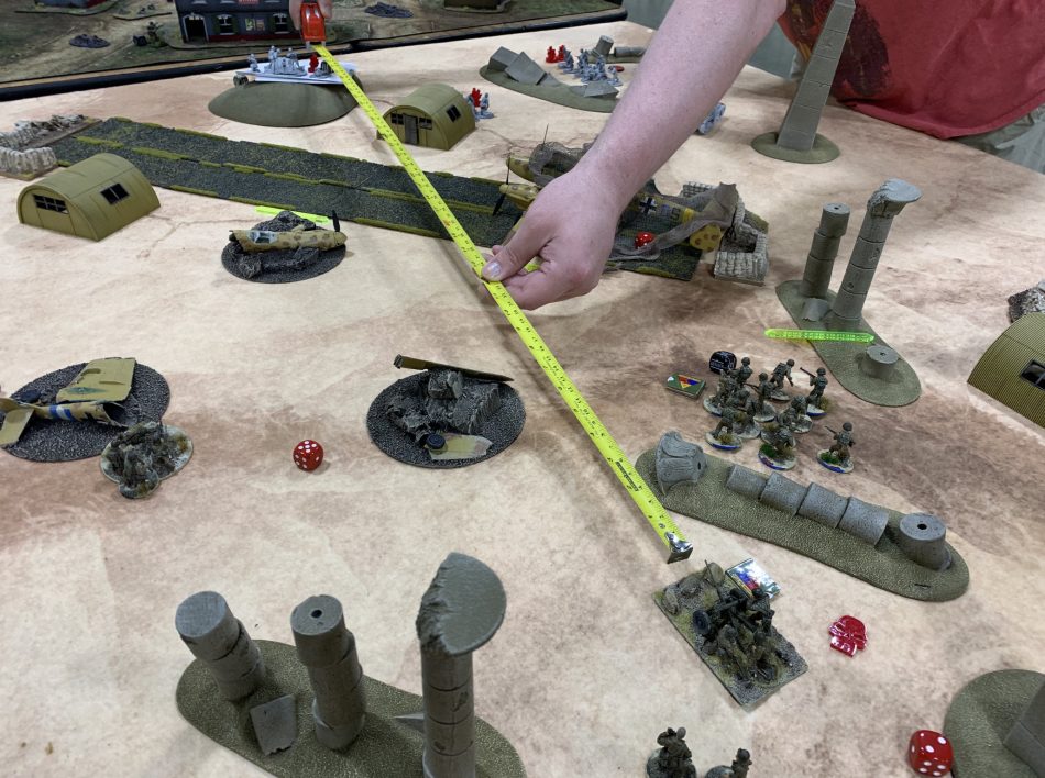 A player extends a tape measure across a table filled with desert terrain in a game of Bolt Action