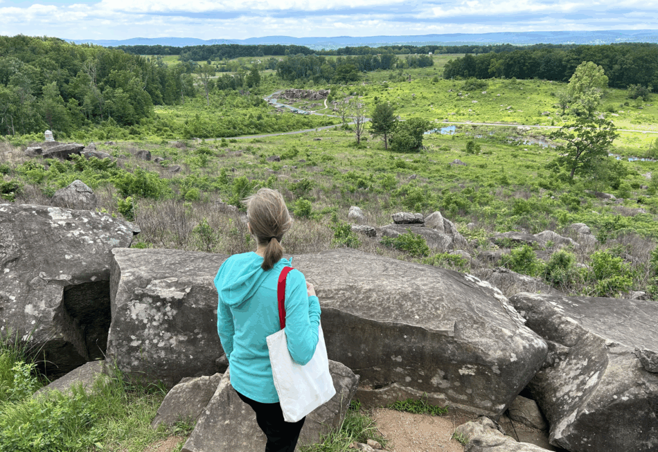 A woman looks out at Devils Den at Gettysburg from the top of Little Round Top
