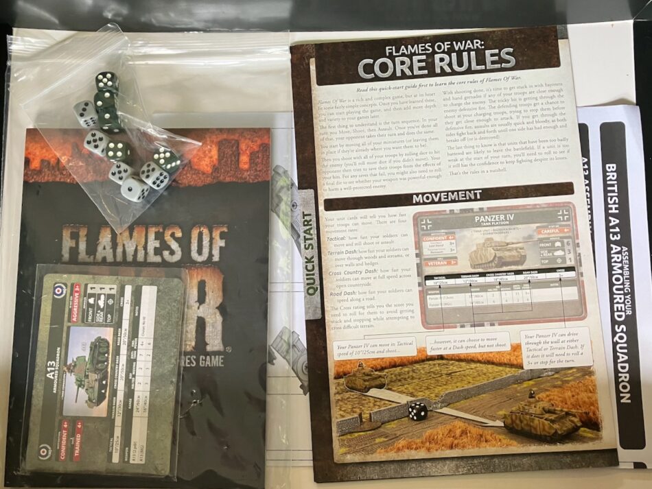 The paper contents of the Dunkirk starter box. Included is as A5 Flames of War rulebook, a back of unit cards, a quick start guide to the game, five grey dice, five olive green dice, and a page of assembly instructions.